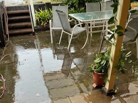 Flooded backyard patio with outdoor furniture sitting in pooled rainwater during a storm