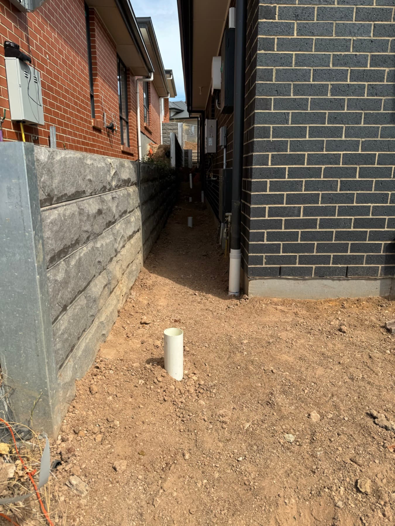 Narrow passage between houses with a hand-dug hole and pipe stub for tank installation