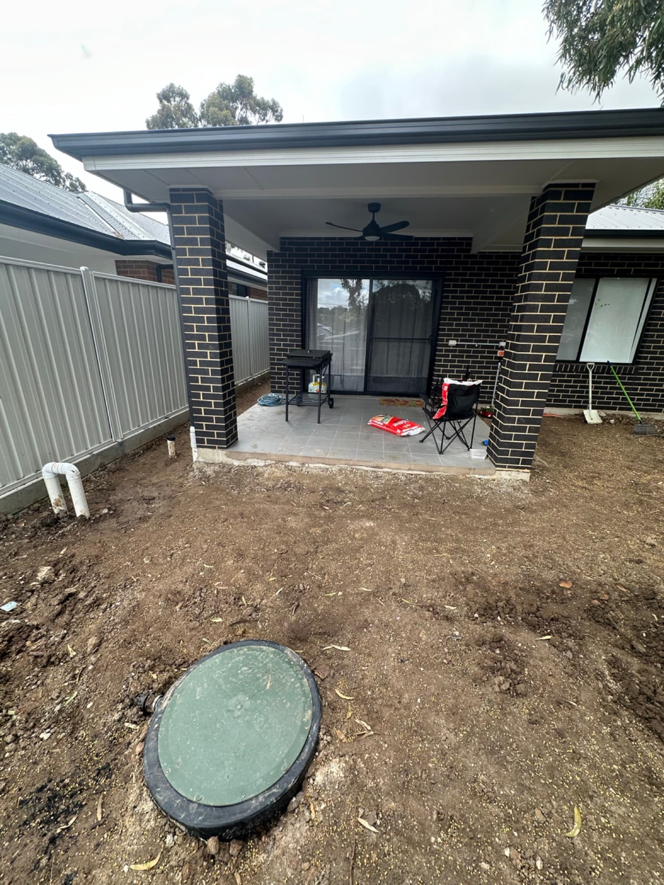 Completed sump pit with green inspection lid installed in front of a new home alfresco area
