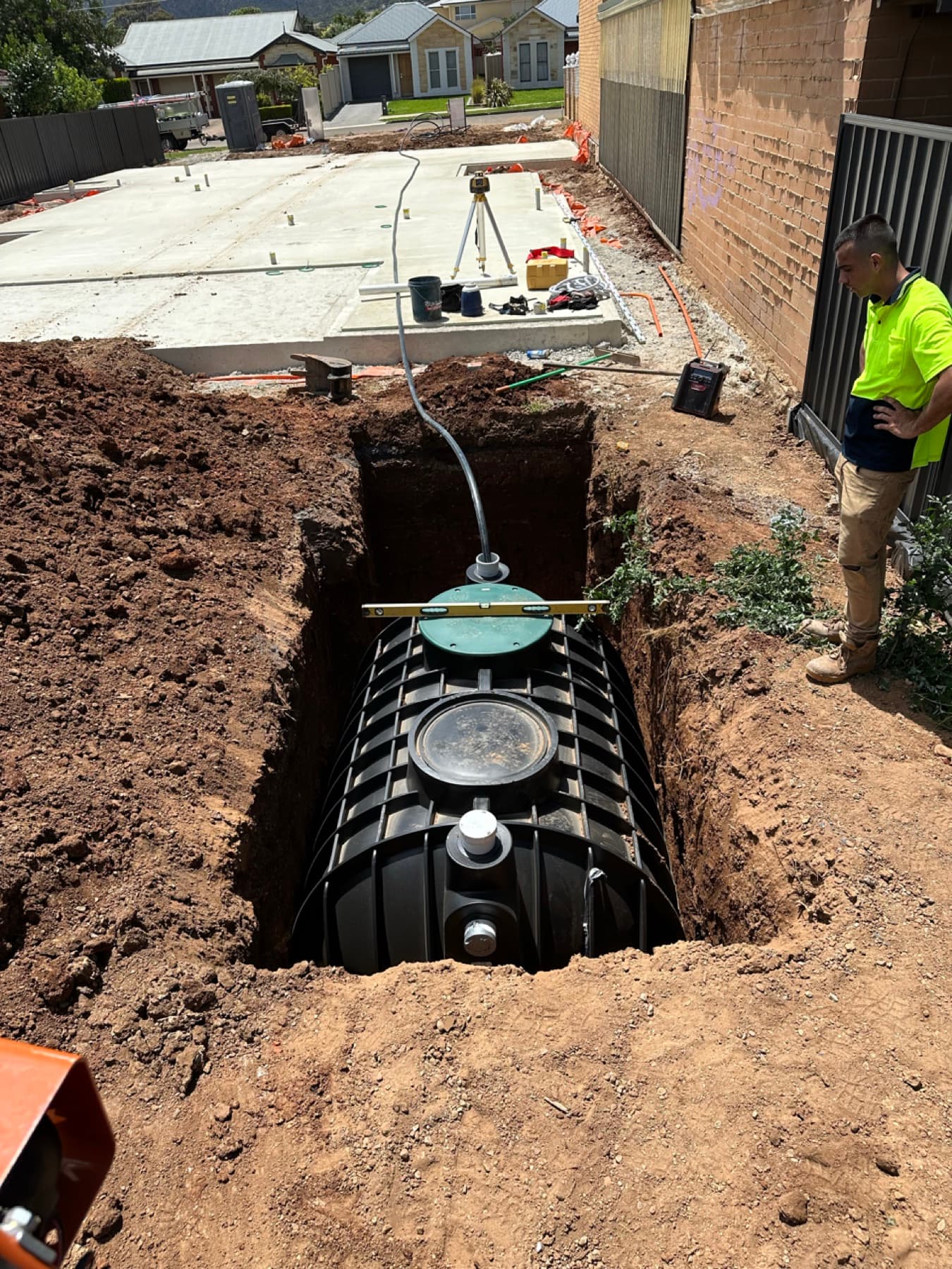 Worker overseeing underground rainwater tank being lowered into an excavated pit on a building site