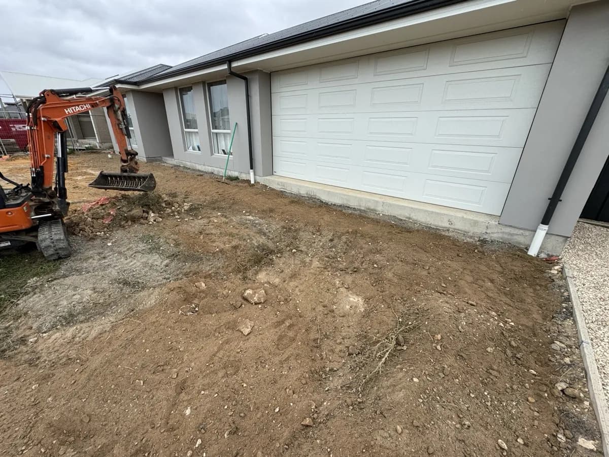 Orange mini excavator levelling the dirt yard in front of a new home's double garage