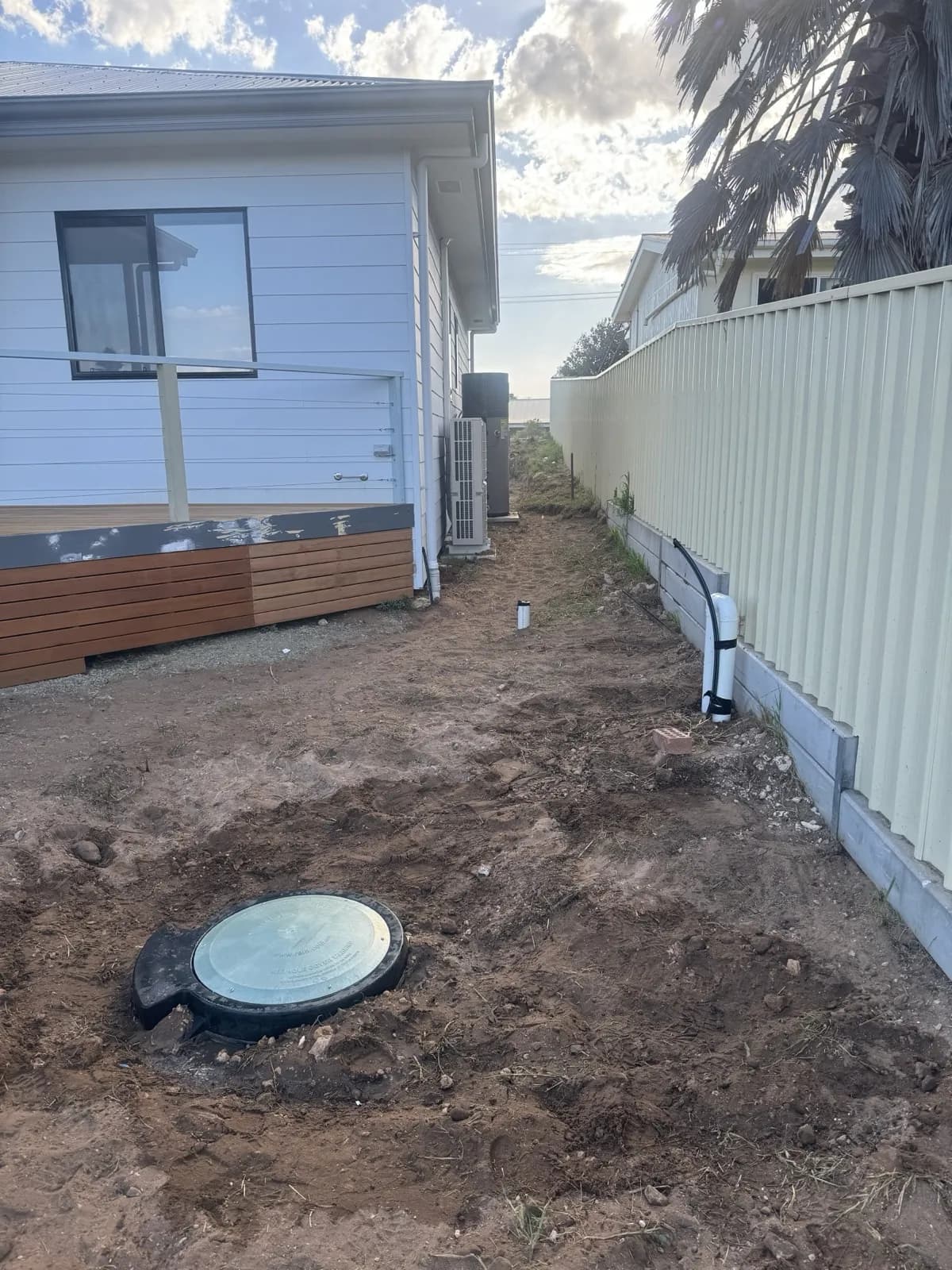 Completed sump pit with a flush inspection lid in a freshly dug side yard beside a new home