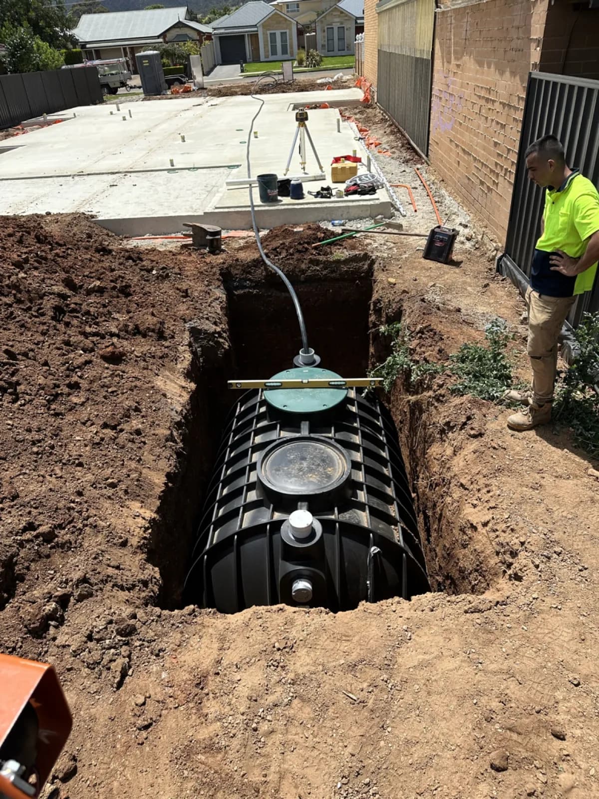 Worker overseeing underground rainwater tank being lowered into an excavated pit on a building site