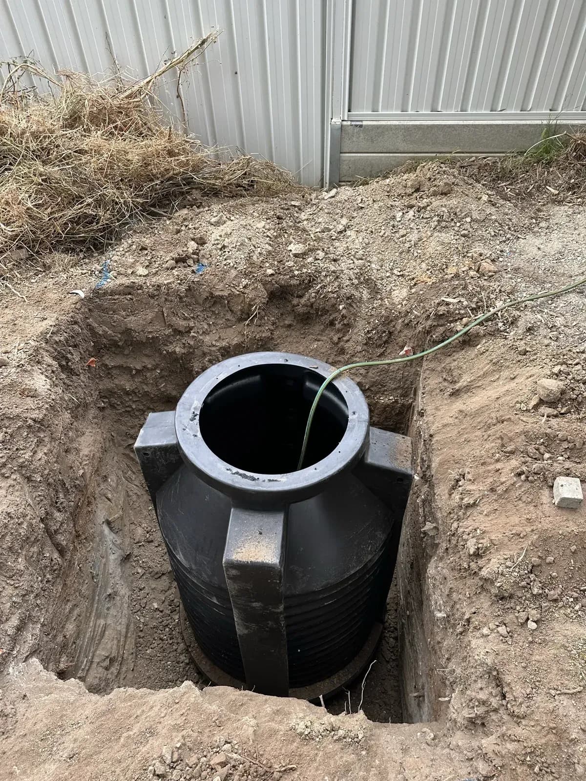 Black poly septic tank seated in an excavated pit during installation
